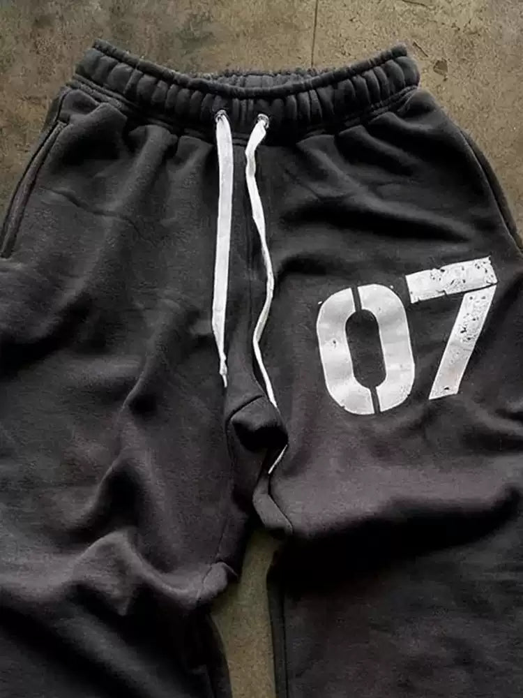 Black sweatpants with a white drawstring and '07' print on a textured surface